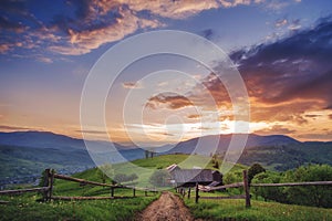 Amazing mountain view. wooden fence, rural road and high mountain village on sunset. summer landscape.  natural