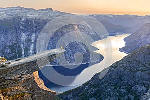 Amazing nature view with Trolltunga and a man sitting on it at sunset under the moon. Location: Scandinavian mountains, Norway, Od