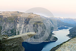 Amazing nature view with Trolltunga and a man sitting on it at sunset under the moon. Location: Scandinavian mountains, Norway,