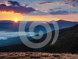 Amazing panoramic landscape in the mountains at sunrise. View of colorful sky and foggy hills covered by forest. Concept of the aw