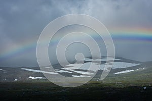 Amazing rainbow in cloudy sky over the tundra landscape on the Arctic Circle line in northern  Norway