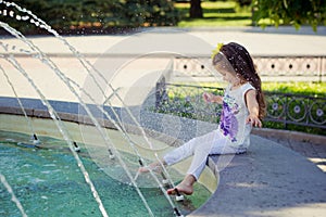 Amazing scene of little fashion baby child girl playing summer time with fountain by ner tiny barefoot legs wearing fancy clothes photo