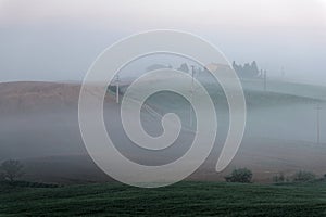 Amazing scenery of idyllic Tuscany countryside with rolling hills veiled in morning fog