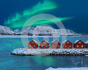 Amazing scenery wit traditional red wooden houses on the shore of Offersoystraumen fjord with Northern Lights