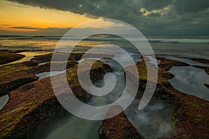 Amazing seascape. Beach with rocks and stones. Low tide. Clear water. Sky reflection in water. Slow shutter speed. Soft focus.