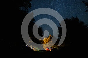 Amazing starry night sky with Milky way and stars above tourists tents in woods in mountains. Camping under the beautiful stars