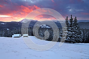 Amazing sunrise. Winter forest. Old wooden huts on the lawn covered with snow. High mountains with snow white peaks. Wallpaper