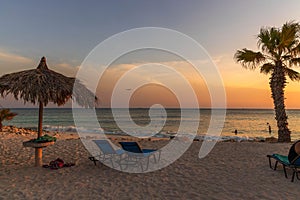 Amazing sunset on sandy beach and Atlantic Ocean. Sun beds and umbrellas on turquoise water and blue orange sky background.