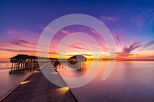 Sunset on Maldives island, luxury water villas resort and wooden pier. Beautiful sky and clouds and beach background for summer va