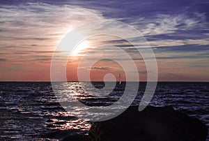 Amazing sunset or sunrise on rocky sea or ocean coast with sailing ship on horizon