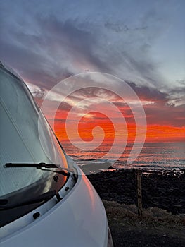 Amazing sunset viewed from outiside a camper van parking on the coast. Freedom and journey alternative vanlife lifestyle. Renting