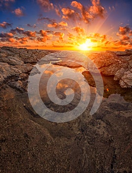 Amazing sunset on the white rocks with sun, blue sky, clouds and reflection in the water, Cyprus