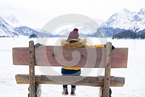 Amazing Swiss Alps viewpoint from wooden bench - happy woman sitting on bench looking snow mountain landscape in front of frozen