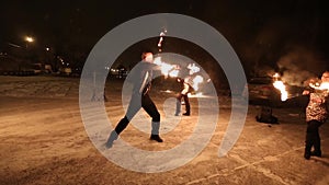 Amazing tribal fire show dance at night on winter under falling snow. Dance group performs with torch lights and