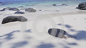 Amazing tropical white sand beach with black rocks and clear blue waves lapping