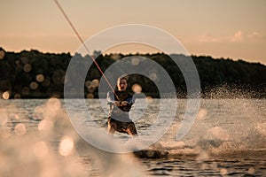 amazing view of attractive man holding rope and energetically riding wakeboard on splashing river wave.