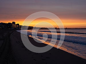 Amazing view of a fiery sunrise with multicolored clouds. Sea waves along the seashore at sunrise