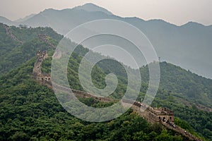 Amazing view from Great Wall of China with a green trees and rocky mountains in the background. Misty foggy air above the hills