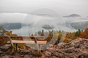 Amazing view of Lake Bled at foggy autumn morning wiyh wooden bench on foreground