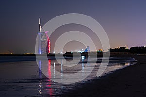 Amazing view to the illuminated Burj al Arab, luxury and modern hotel in Dubai. Colorful lights reflects over the water.