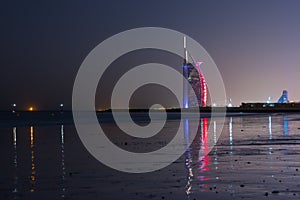 Amazing view to the illuminated Burj al Arab, luxury and modern hotel in Dubai. Colorful lights reflects over the water.