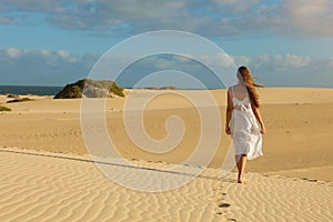 Amazing view of young woman walking barefoot on desert dunes at sunset in Corralejo, Fuerteventura