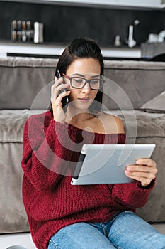 Amazing woman indoors in home on sofa using tablet computer talking by mobile phone