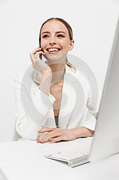 Amazing woman sitting isolated over white wall background using pc computer talking by mobile phone