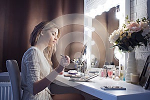 Amazing young woman doing her makeup in front of mirror. Portrait of beautiful girl near cosmetic table