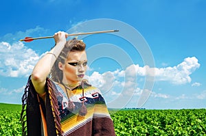 Amazon girl aggressive makeup, in a poncho, cosplay in the field, holds a bow and arrow. Paganism, feminism, independence, tribe