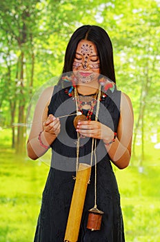 Amazonian exotic woman, facial paint, black dress, case for arrows and small wooden bottle hanging around neck, applying