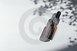 Amber bottle with cannabis oil used for medical purposes. White background with daylight and flowers shadows.