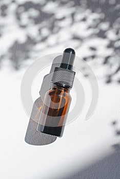 Amber bottle with cannabis oil used for medical purposes. White background with daylight and flowers shadows.