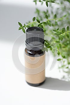 Amber bottle with craft label thyme essential oil. White background with daylight and beautiful shadows