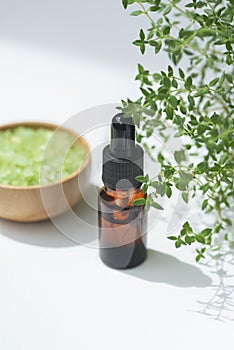 Amber bottle with dropper pipette and serum or thyme essential oil. White background with daylight and beautiful shadows