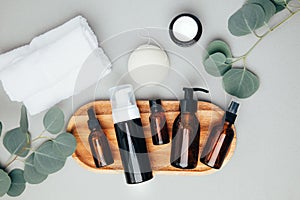 Amber bottles with facial cosmetics, sponge and white towels on a tray with a branch of eucalyptus