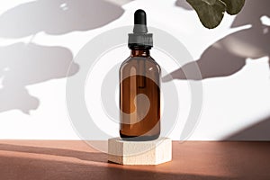 Amber cosmetic bottle on wooden geometric pedestal podium, product packaging with natural shadows from plants, anti