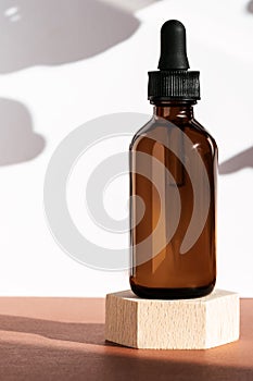Amber cosmetic bottle on wooden geometric pedestal podium, product packaging with natural shadows from plants, anti