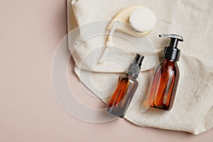 Amber glass bottles with body lotion and shampoo and facial cleansing brush on beige background. Skin care concept