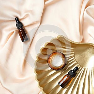 Amber glass cosmetic bottle, moisturizer cream and golden seashell on peach silk background