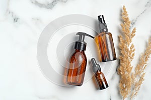 Amber glass cosmetic bottles and dry flowers on marble background. Set of natural organic SPA beauty products