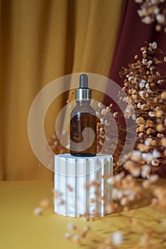Amber glass dropper bottle with metallic lid on white podium.