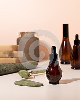 Amber glass spray and dropper bottles with cosmetic on light bathroom table. Natural jade roller for facial massage and