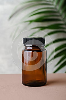 Amber glass supplement bottle and tropical green leaf. Medical package for pills, capsule, drugs. Herbal medicine concept photo