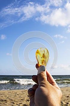 Amber. Very beautiful transparent amber in the palm of your hand. On the sandy beach lies a hand with an amber stone