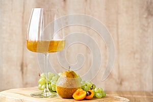 Amber or white wine with fruit. Poured glass with wine surrounded by grapes, peaches and pears