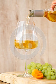 Amber or white wine with fruit. Poured glass with wine surrounded by grapes, peaches and pears