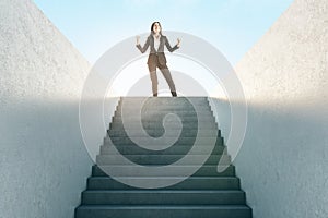 Ambition concept with joyful businesswoman in black suit on top of stairway on sky background