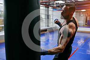Ambitious boxer man hiting heavy bag at gym