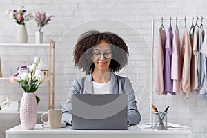 Ambitious businesswoman with glasses working with laptop in interior of fashion studio